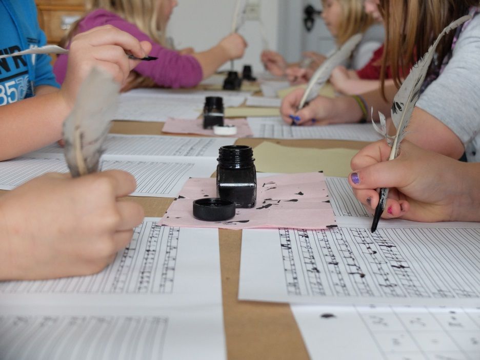 Kinder sitzen am Tisch und schreiben mit Feder und Tinte wie früher, konzentriert über ihr Papier gebeugt.